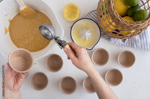 Fotografie Right woman hand holding an ice cream scoop ready to fill it with a muffin batter and holding an empty bakery cup with the left hand
