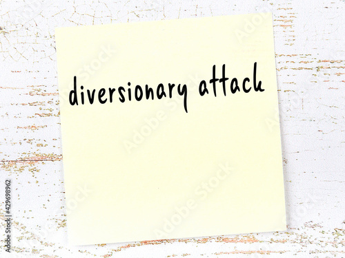 Yellow sticky note on wooden wall with handwritten word diversionary attack photo