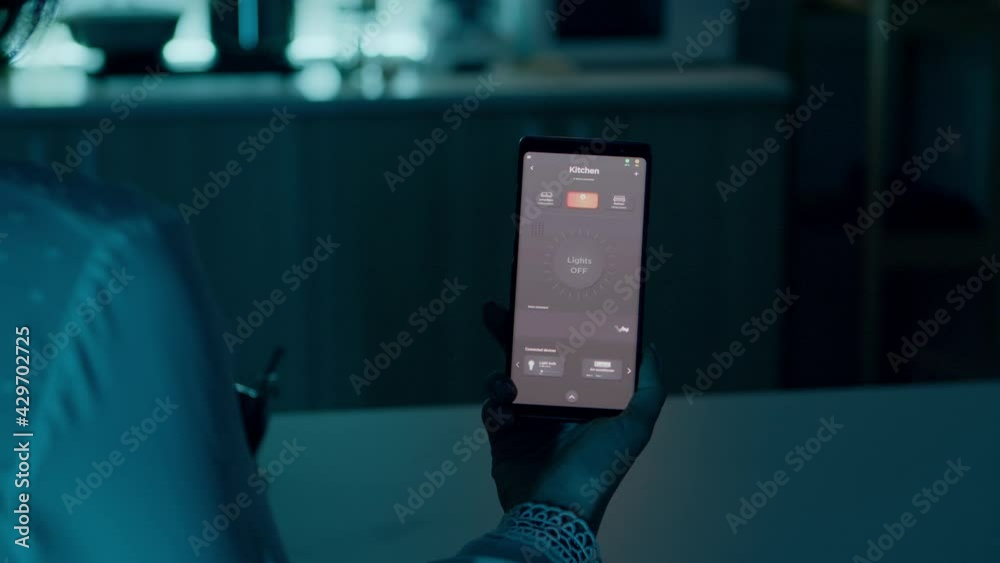 Woman sitting in house with automation light system holding smartphone turning on light using voice activated application. Person controlling room ambiance and energy efficiency with smart home app
