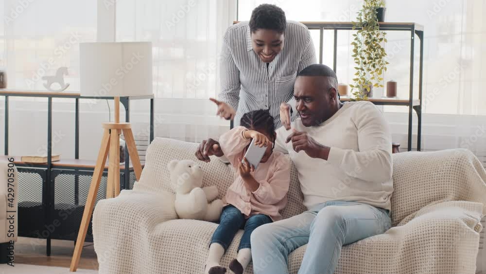 Afro american man father grandfather with little girl daughter child playing mobile online video games on phone sitting on sofa young black mother angry african woman screaming swears, family conflict