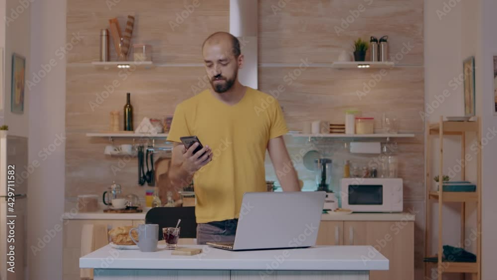 Young person coming in kitchen holding mobile giving voice command to smart home application and lights turning on. Man using smartphone with high tech wireless app software controlling room ambiance