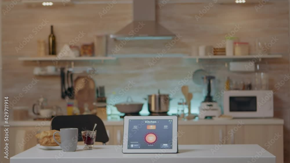 Smart application on tablet placed on kitchen desk in empty house automation system, turning on the light. Notepad with wireless lighting controlling, high tech to monitoring electricity effiency