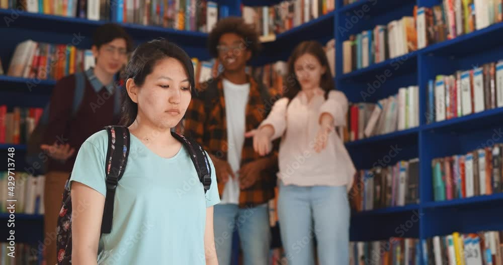Diverse students bullying and laughing at sad asian young woman in library Diverse students bullying and laughing at sad asian young woman in library