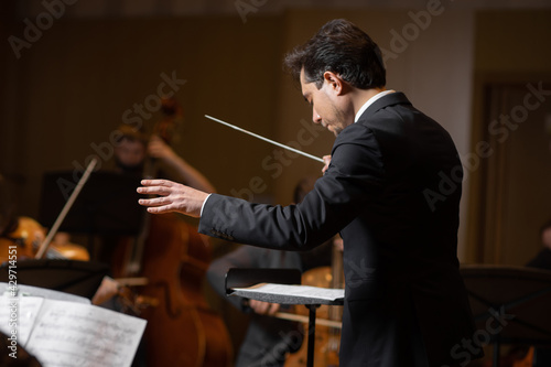 Conductor of symphony orchestra with performers in background in concert hall photo