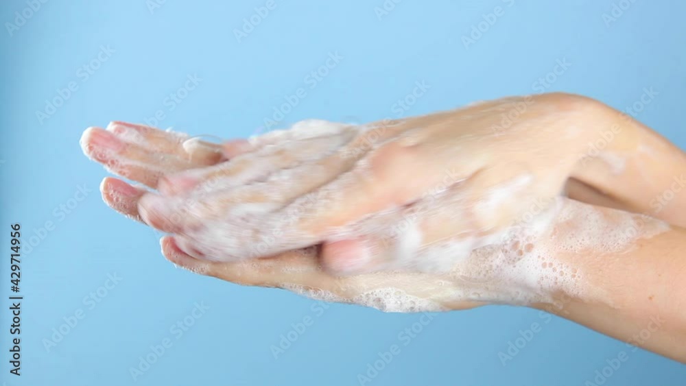 A woman lathers and washes her hands on a blue background close-up. A woman lathers and washes her hands on a blue background close-up.