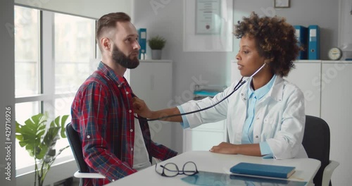 Female doctor examining patient heart beat with stethoscope in office.
