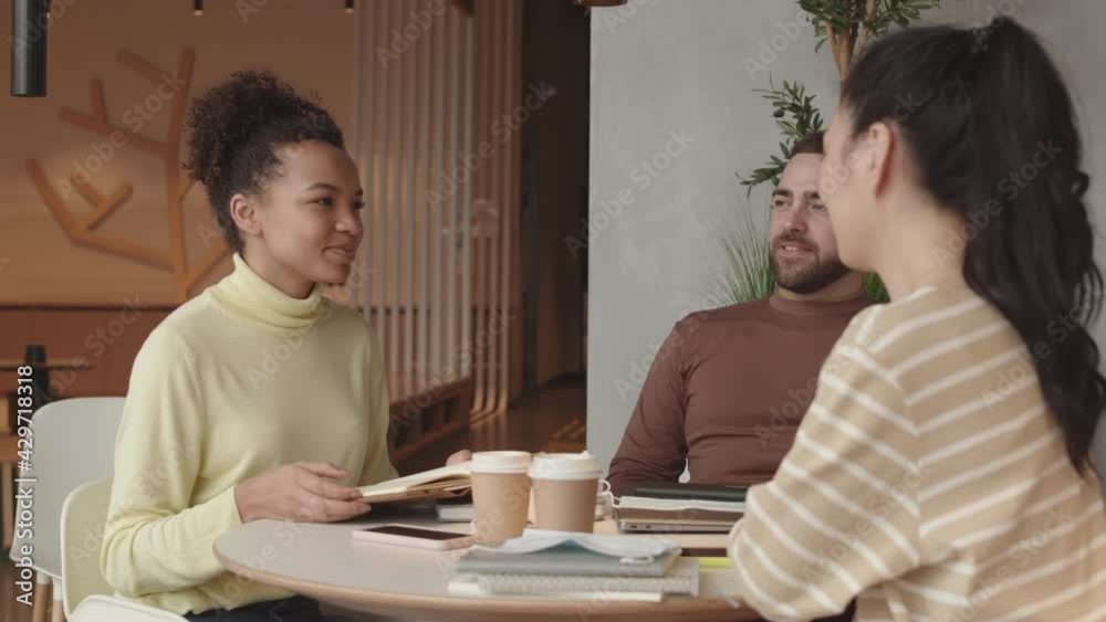 Arc shot of young Asian and Mixed-Race women and Caucasian man sitting at round table in restaurant, smiling and talking
