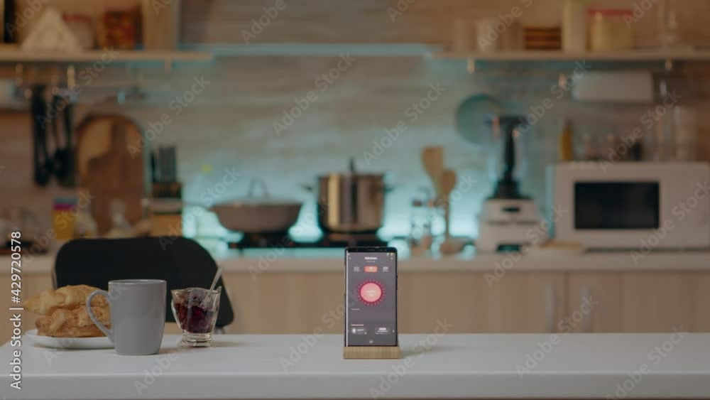 Phone with intelligent software placed on table in kitchen with nobody in, controlling light with high tech application. Mobile with smart home app in empty house automation system