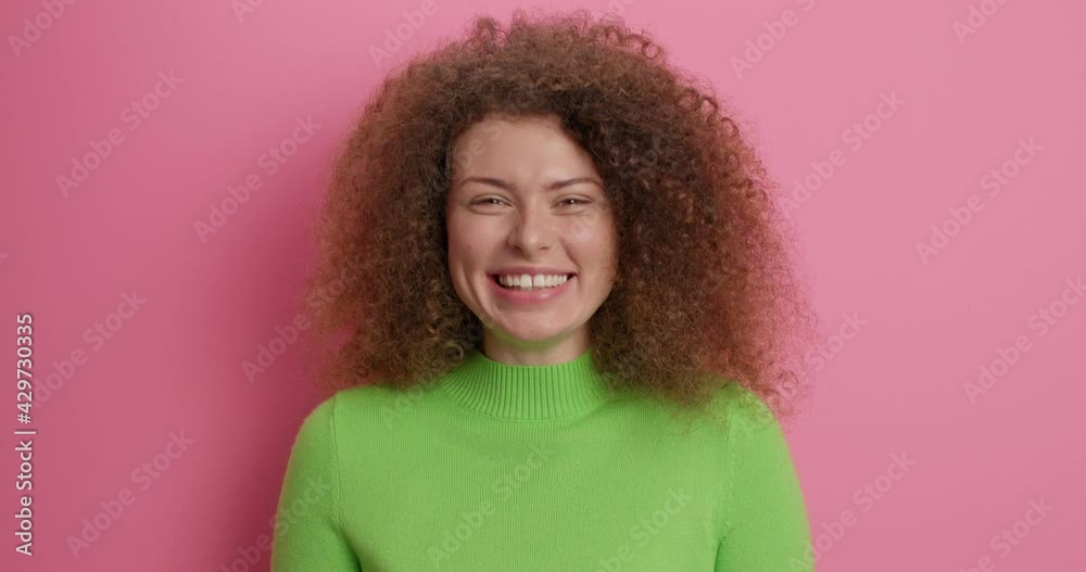 Glad smiling young woman shows okay gesture in approval winks eye says yes or no problem makes alright gesture approves choice dressed in casual green turtleneck models against pink background