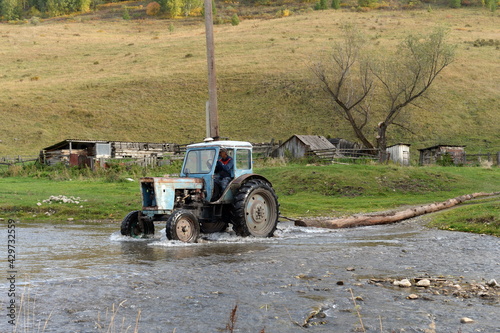 MTZ-80 tractor drags a tree trunk across the mountain river Yarovka in the taiga village of Generalka, Altai Krai photo