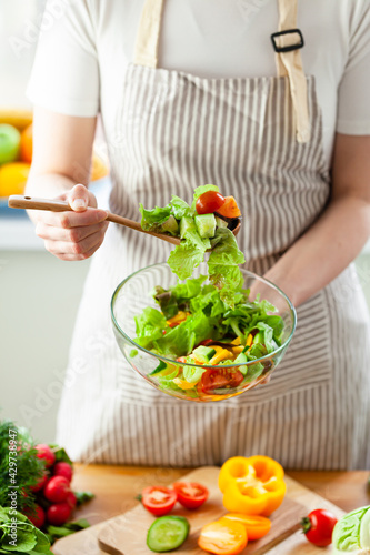 Beautiful young woman preparing delicious fresh vitamin salad. Concept of clean eating  healthy food  low calories meal  dieting  self caring lifestyle. Colorful vegetables  glass bowl. Close up