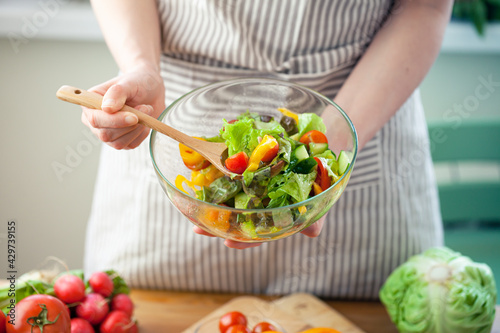 Beautiful young woman preparing delicious fresh vitamin salad. Concept of clean eating, healthy food, low calories meal, dieting, self caring lifestyle. Colorful vegetables, glass bowl. Close up