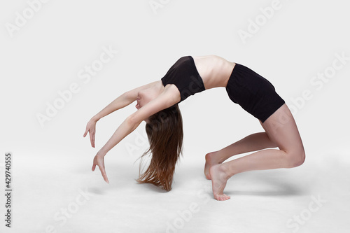 Young slim athletic girl, with long hair, in a black top and shorts, in the studio on a white background