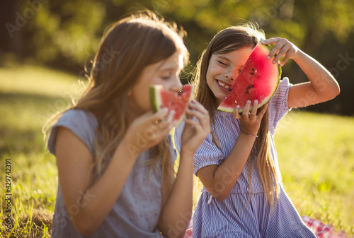 Two little girls spending time outside and eating watermelon. Focus is on background.