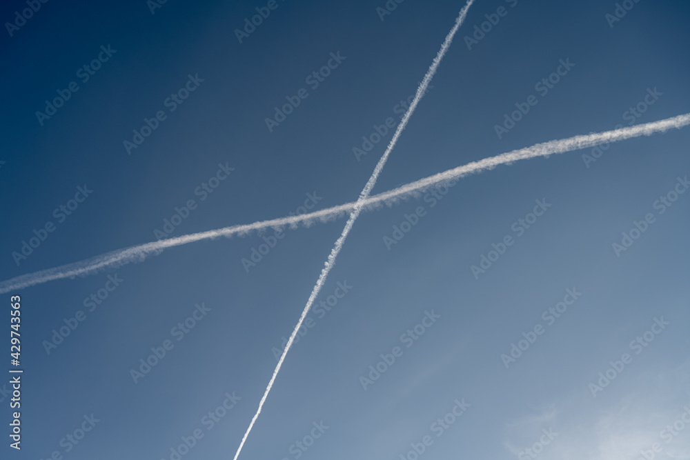 White trails, from jet exhaust, form a cross in the sky. A blue sky on the background White trails, from jet exhaust, form a cross in the sky. A blue sky on the background