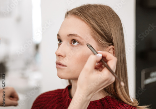 makeup artist applies eye shadow to the eyelids on a beautiful young woman blonde model  face make up concept