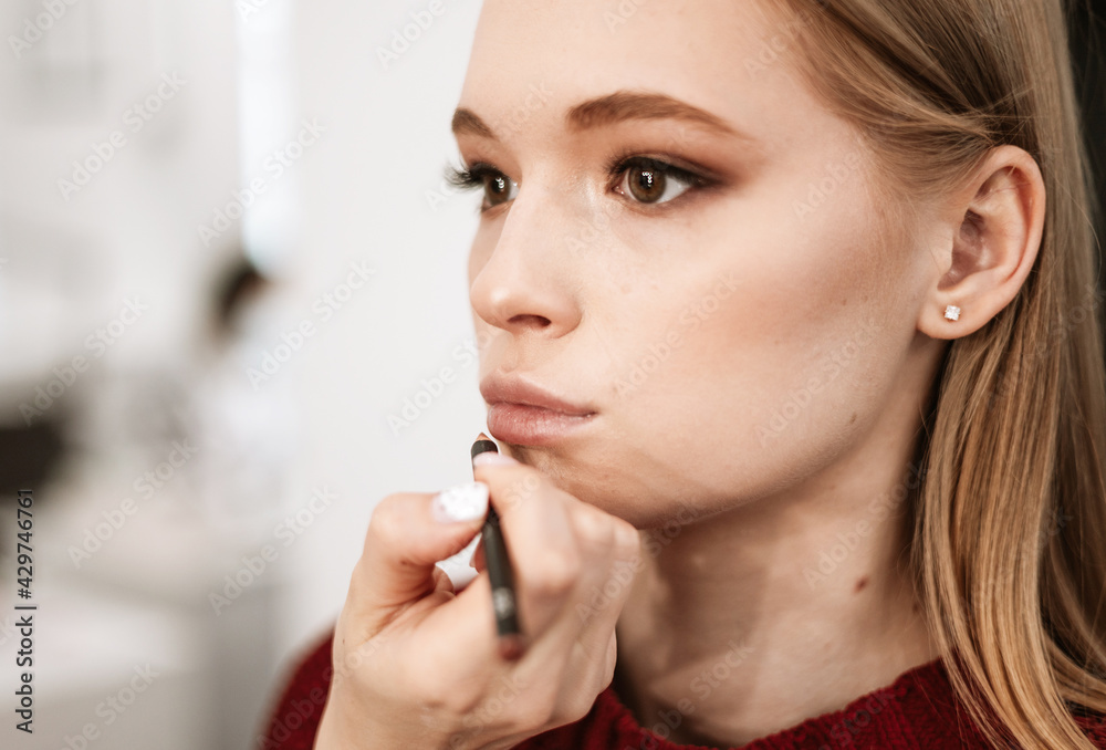 makeup artist paints lips with lipstick with a brush on a beautiful young woman blonde model, face make up concept makeup artist paints lips with lipstick with a brush on a beautiful young woman blonde model, face make up concept