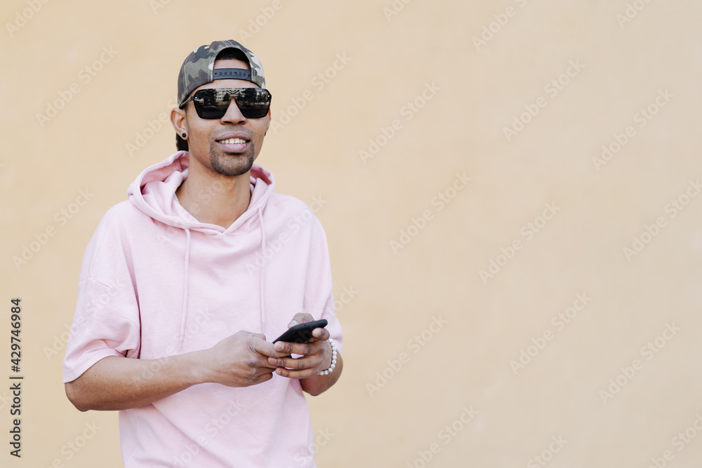 Fototapeta premium Smiling young man guy in pink t-shirt posing on yellow wall background portrait. People lifestyle concept. Mock up copy space. Using mobile phone, typing sms message