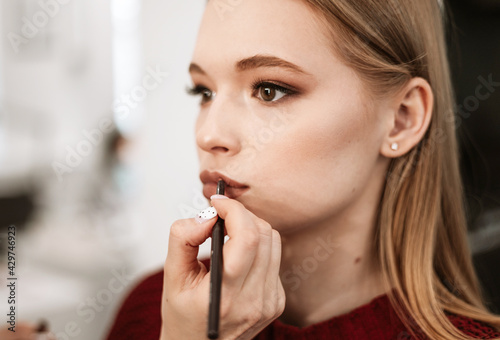 Fototapeta Naklejka Na Ścianę i Meble -  makeup artist paints lips with lipstick with a brush on a beautiful young woman blonde model, face make up concept