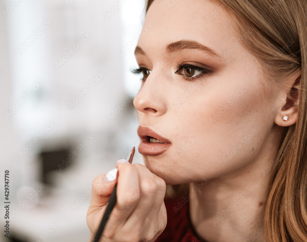 makeup artist paints lips with lipstick with a brush on a beautiful young woman blonde model, face make up concept makeup artist paints lips with lipstick with a brush on a beautiful young woman blonde model, face make up concept