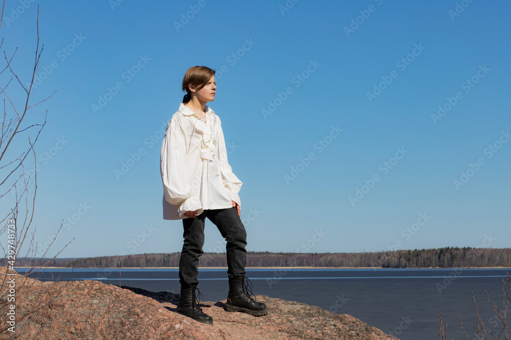 Boy standing on a granite rock against a background of blue sky and water