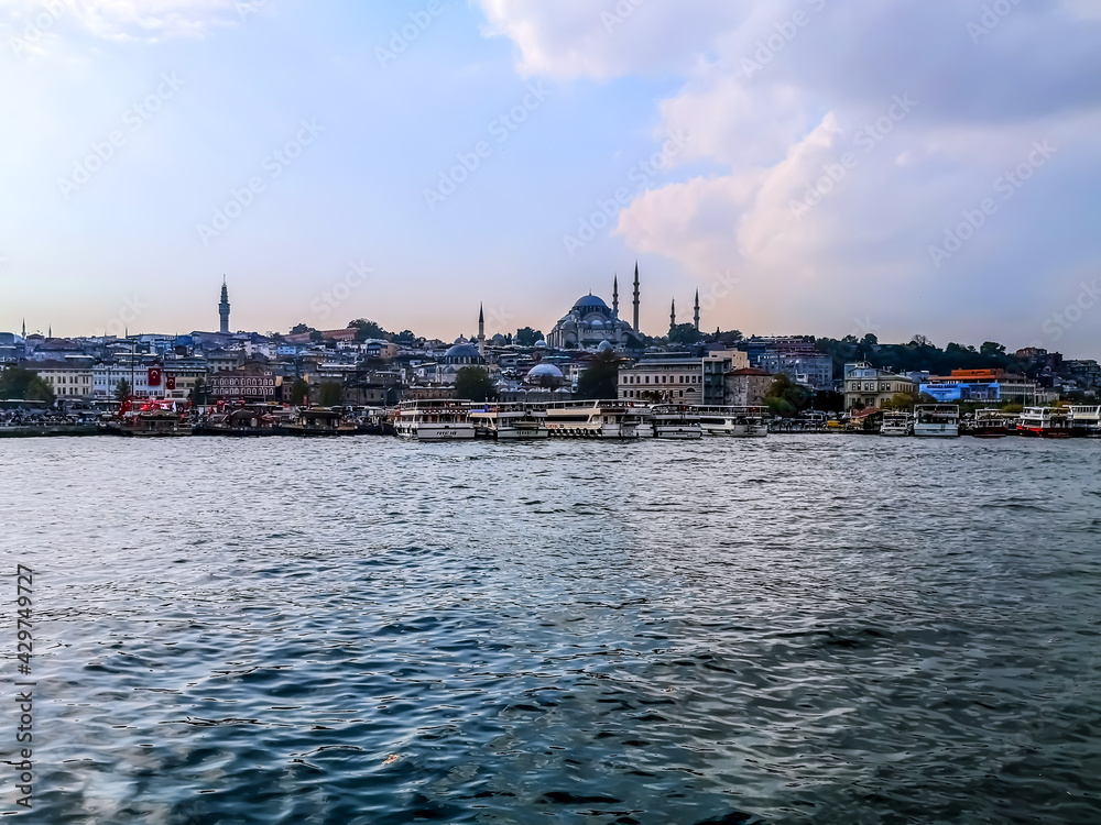 Naklejka premium Istanbul, Turkey - October 29, 2019: View from the Golden Horn bay to the Eminonu district in Istanbul. City panorama with ships moored at the coast and the Suleymaniye Mosque on the horizon