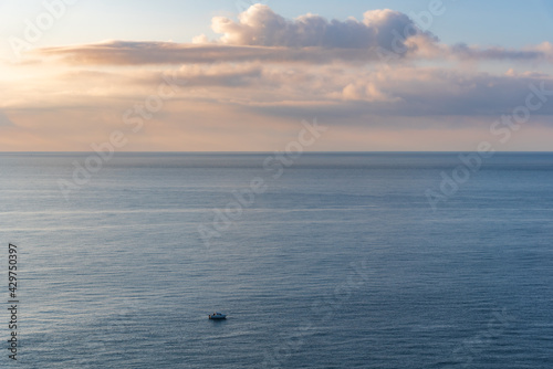 Fotografie Small boat in front of the immensity of the sea, with clouds in the sky at dawn