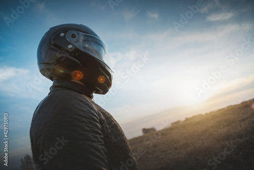 A motorbiker stands among the field and looking at sunset. © Dmitriy