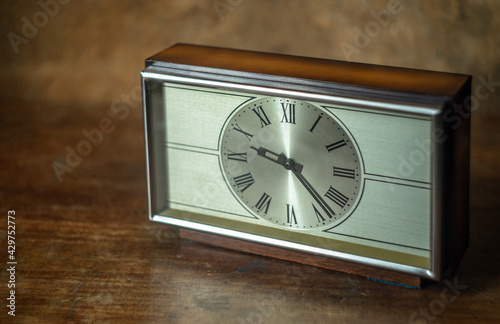 An old mechanical mahogany clock sits on a wooden table