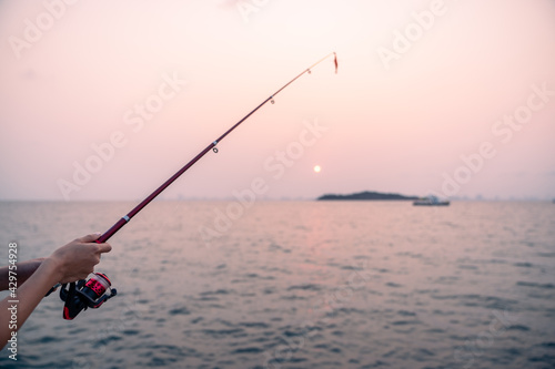 Woman hand holding fishing rod with sea background, fishing at sunset. © marchsirawit