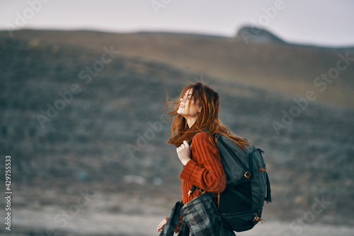 woman in red sweater with backpack looks back on nature in the mountains