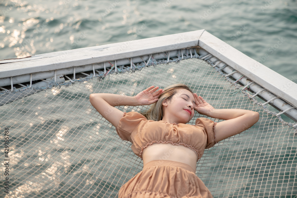 Woman lying on a pier with sea background, sit on the net by the sea.