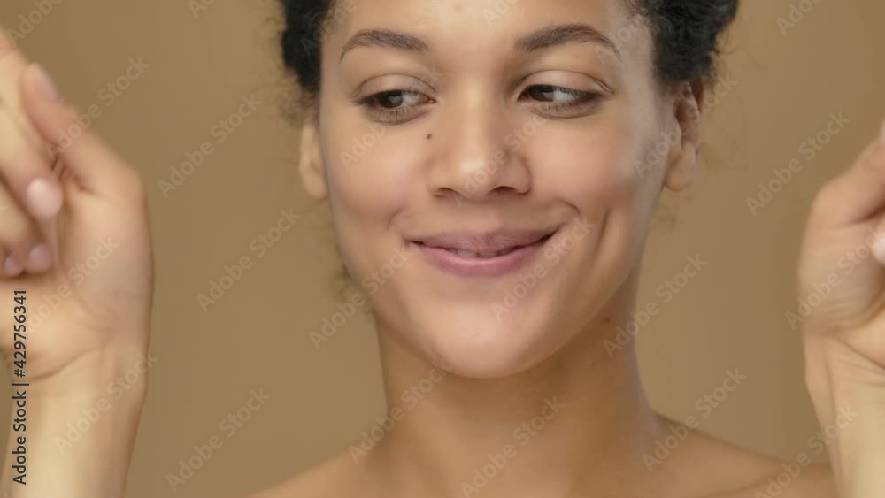 Beauty portrait of young African American woman smiling and showing heart with fingers. Black female model posing on brown studio background. Close up. Slow motion ready, 4K at 59.94fps.