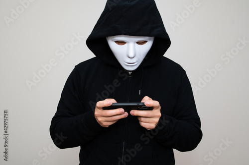 Hacker with anonymous mask playing game with his phone