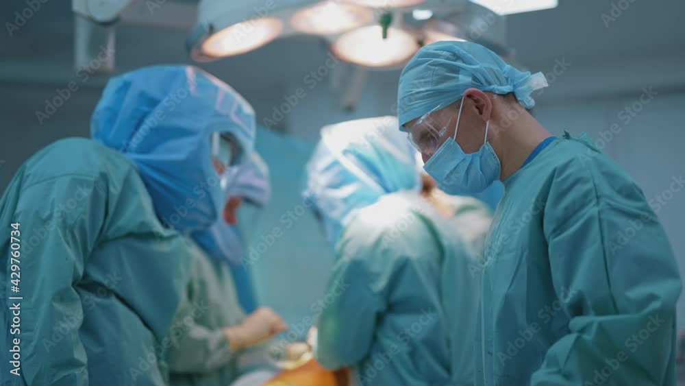 Team of surgeons operating infected patient. Group of doctors in safety suits working in the operating room. Male assistant in mask help medical specialists. Covid 19. Team of surgeons operating infected patient. Group of doctors in safety suits working in the operating room. Male assistant in mask help medical specialists. Covid 19.