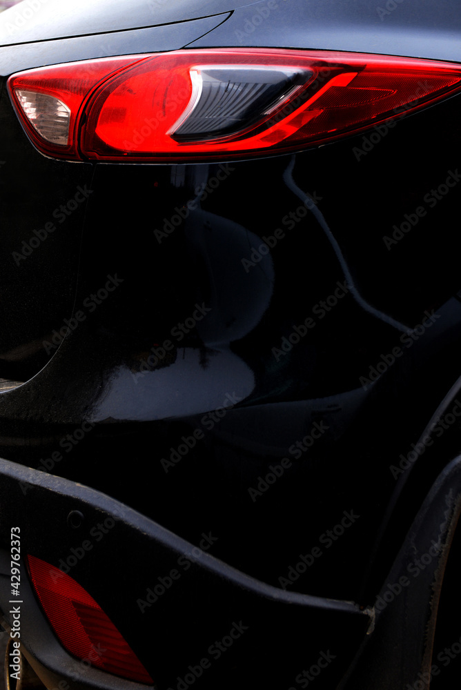 Fototapeta premium Black car with red headlight close-up, rear view, side view. An abstraction.