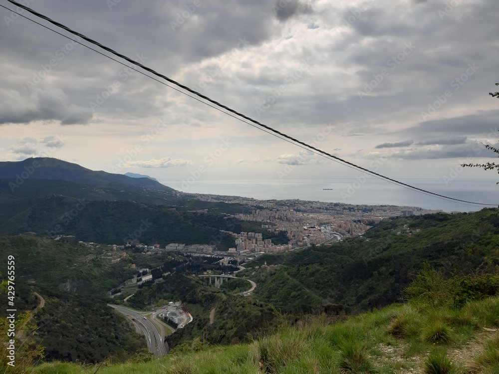 Discovering the mountains around Genoa. Panoramic view to the city. Grey sky in the background. First green leaves in spring. Discovering the mountains around Genoa. Panoramic view to the city. Grey sky in the background. First green leaves in spring.