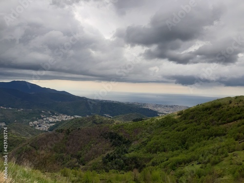 Discovering the mountains around Genoa. Panoramic view to the city. Grey sky in the background. First green leaves in spring.