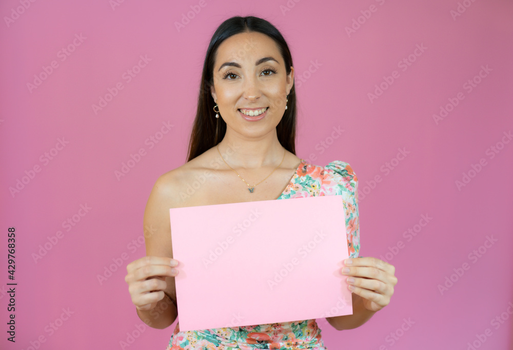 Young beautiful woman smiling and holding a blank sheet of paper isolated over pink background. Young beautiful woman smiling and holding a blank sheet of paper isolated over pink background.