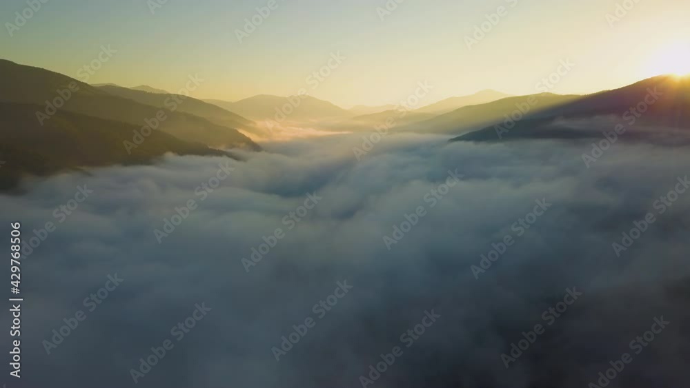 Aerial view of vibrant sunset over white dense foggy clouds with distant dark silhouettes of mountains on horizon. Aerial view of vibrant sunset over white dense foggy clouds with distant dark silhouettes of mountains on horizon.