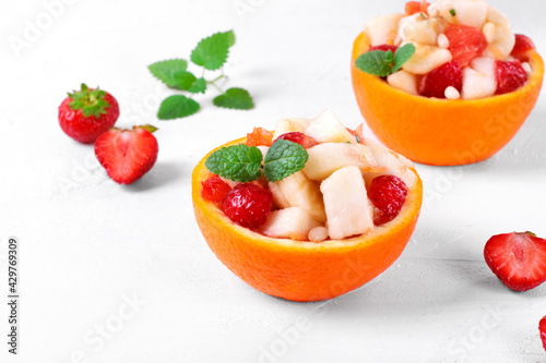 Fruit salad served in orange half. Orange, pear, apple, banana, strawberry, pine nut and mint chopped and mixed in the organic bowl