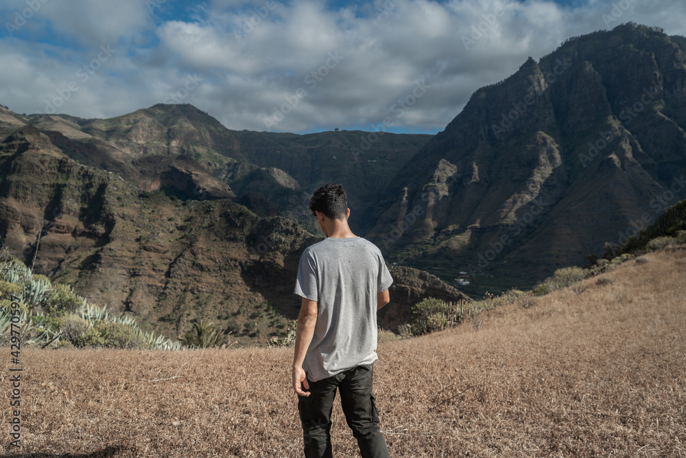 young man walks through a meadow towards the edge of the mountain. Agaete Valley. Gran canaria young man walks through a meadow towards the edge of the mountain. Agaete Valley. Gran canaria