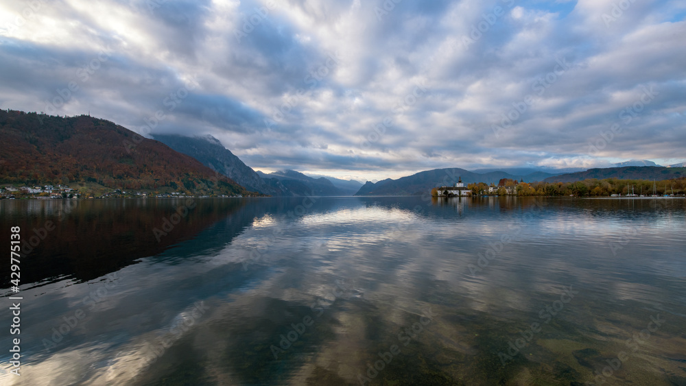 Fototapeta premium Traunsee mit Traunstein und Schloß Ort im Hintergrund früh morgens im Herbst mit dramatischen Wolken, die sich im Wasser spiegeln, Oberösterreich