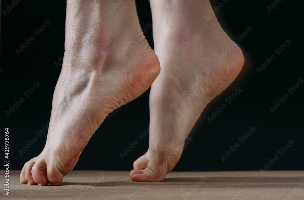 Close up low key of bare foot dancer lifting on tip toes, on black background Close up low key of bare foot dancer lifting on tip toes, on black background