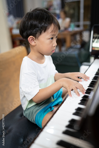 A boy is studying piano online with tablet.