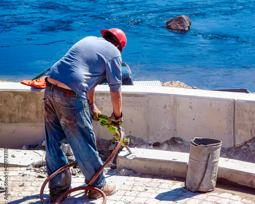 Construction worker with jackhammer working on a cement retaining wall. Room for text  photo