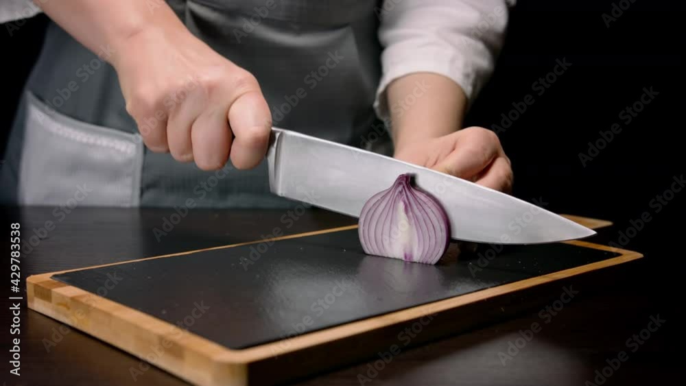 Female hands cutting in slices red onion with knife on cutting board. Close up