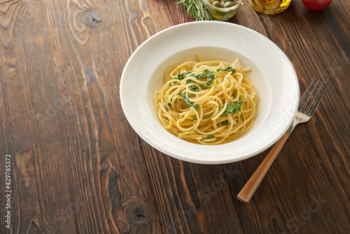 Spaghetti pasta with spinach leaves and cheese on a white plate on the wooden background, top view from above