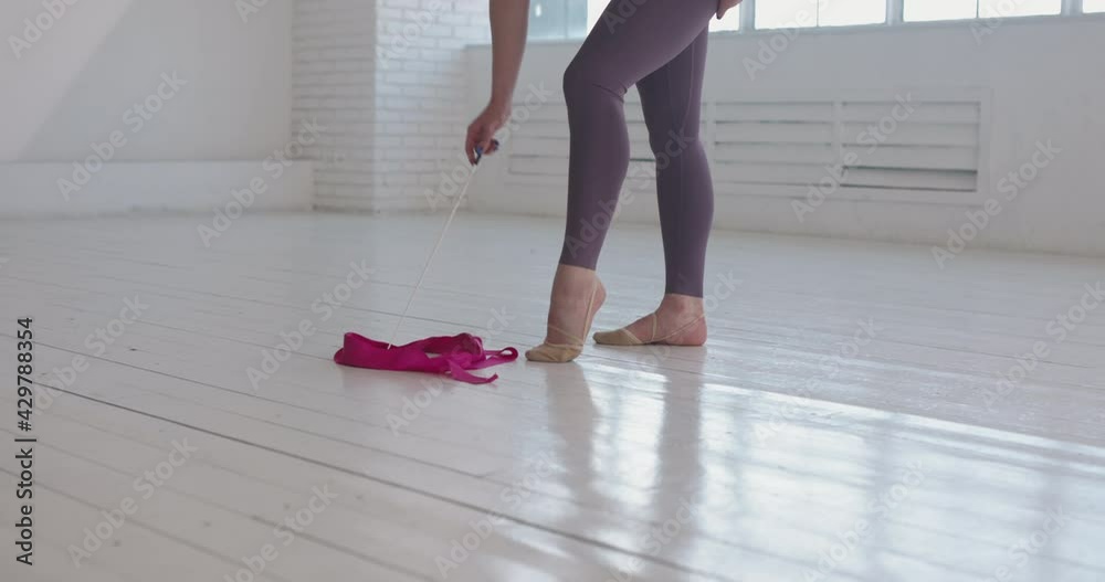 Fit rhythmic gymnast putting down pink ribbon, fixing her pointe shoes than looking at camera. Portrait of beautiful athlete 4k footage Fit rhythmic gymnast putting down pink ribbon, fixing her pointe shoes than looking at camera. Portrait of beautiful athlete 4k footage