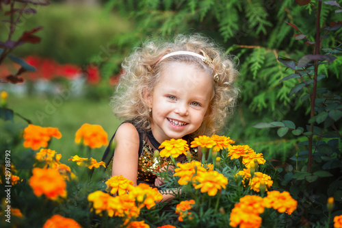 Little laughing girl with curly blond hair plays with flowers in summer park